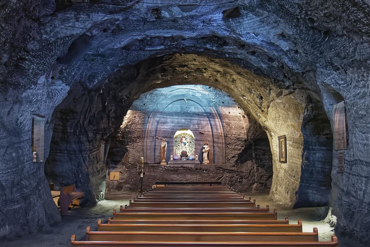 Underground chapel with rows of wooden benches and a salt-carved altar inside a dark, rocky cavern.