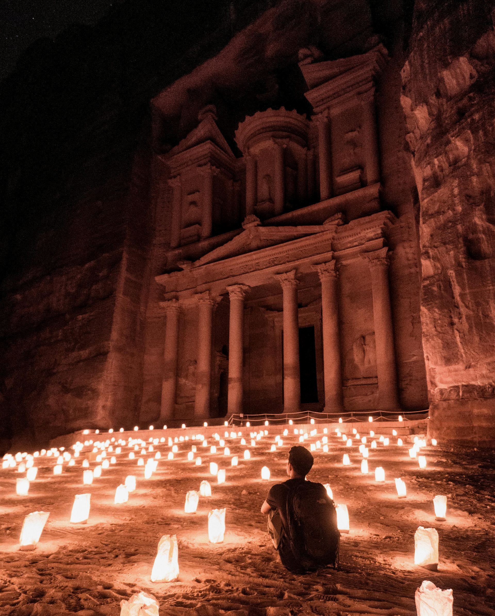 Man sits before lit candles illuminating the Treasury in Petra, Jordan, at night.