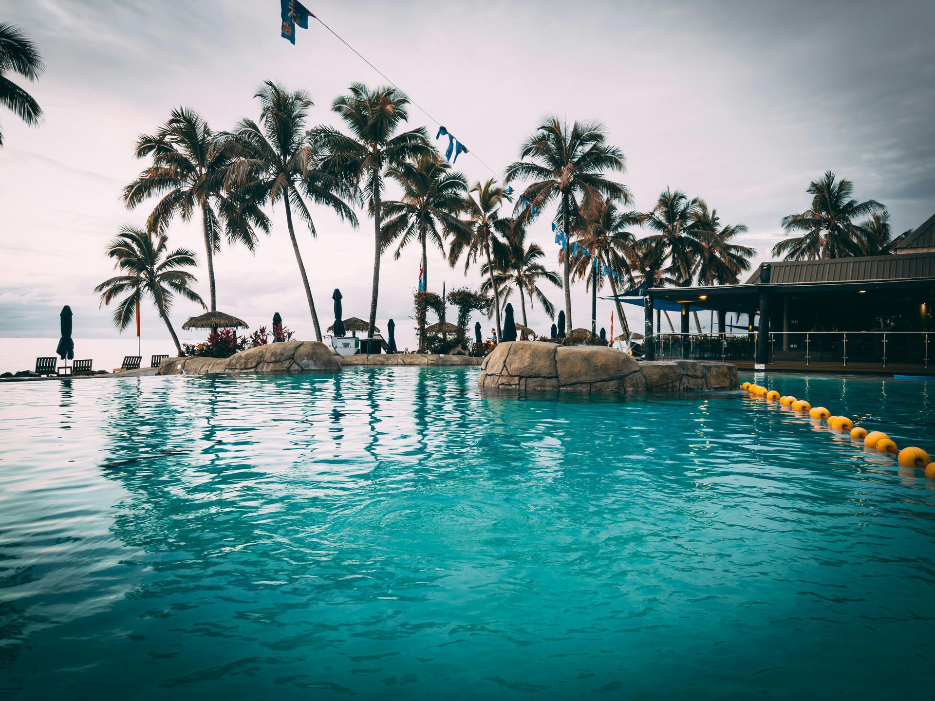 Pool of turquoise water with palm trees and a cloudy sky in the background.