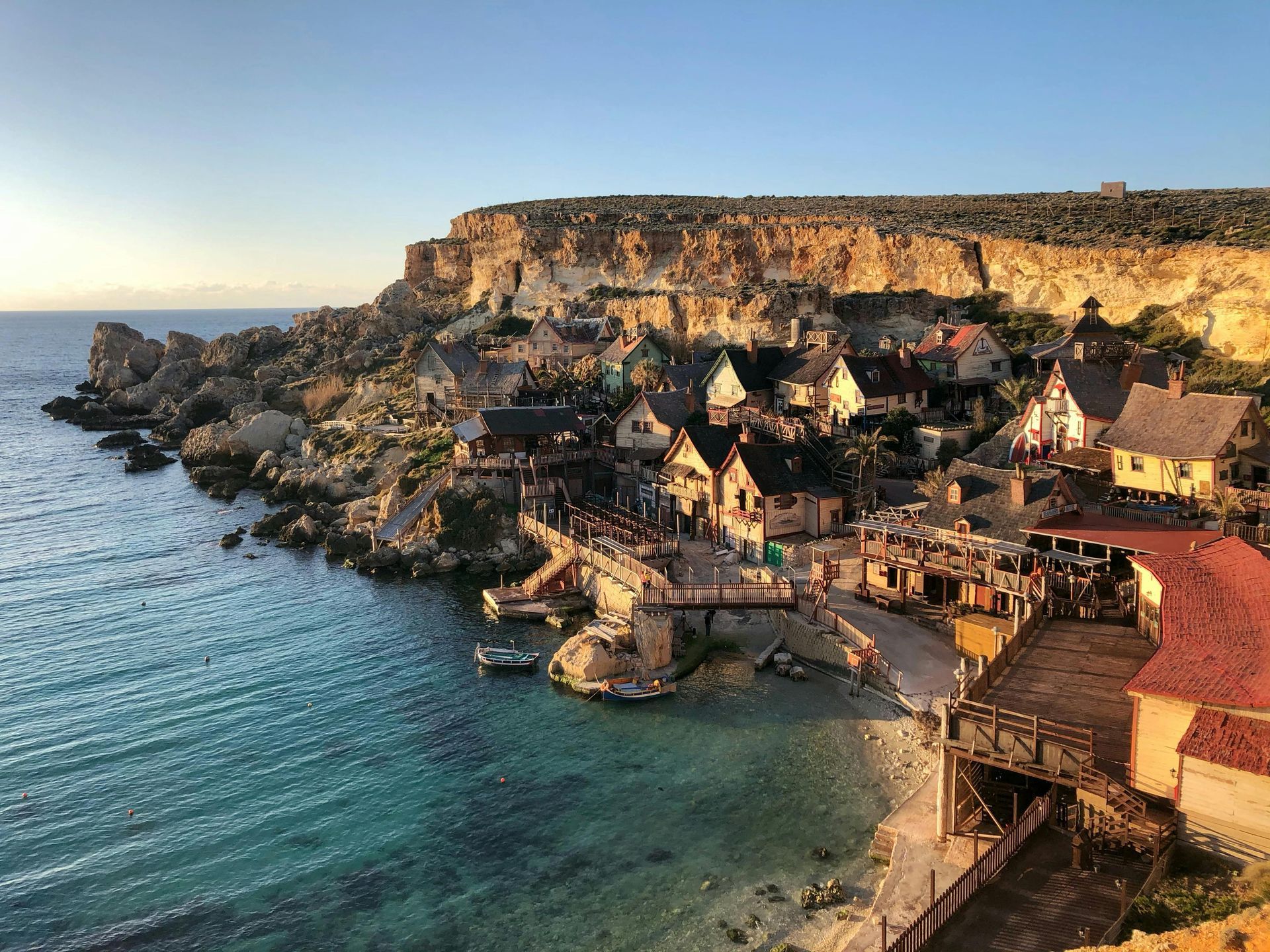 Village nestled in a cove with colorful buildings, cliffs, and clear turquoise water. Malta, Mediterranean