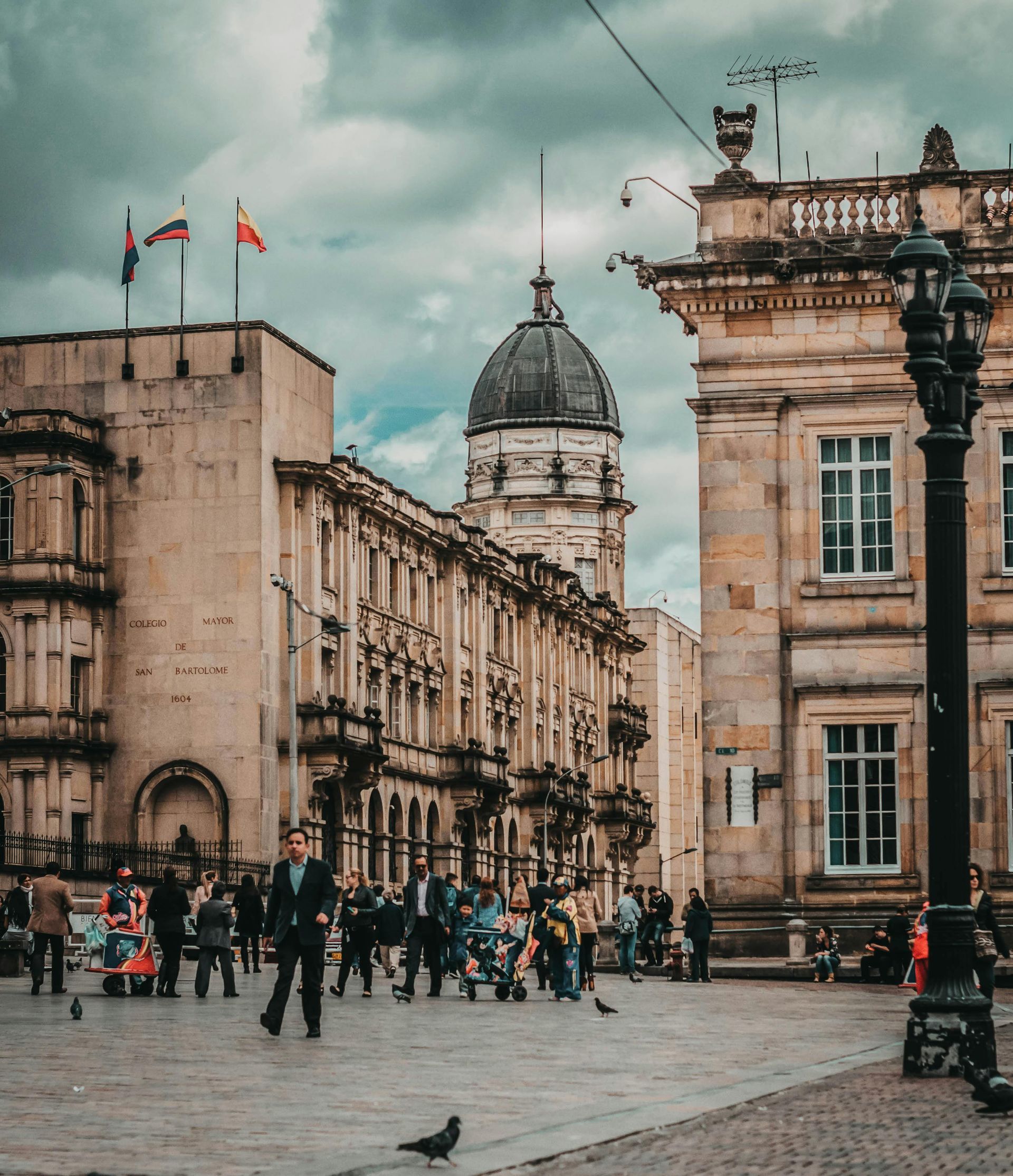 Large plaza in front of historic buildings, people walking, overcast sky.
