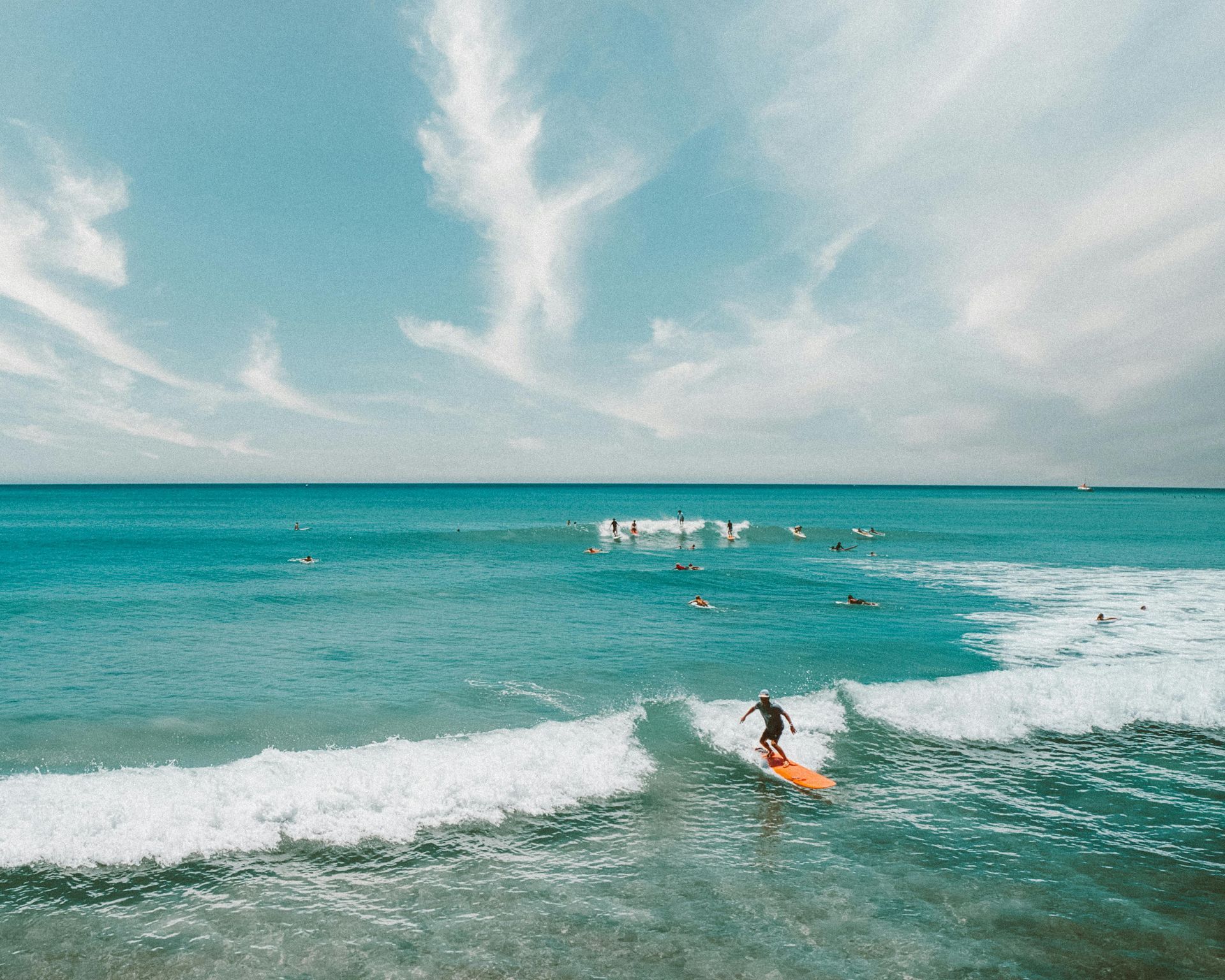 Surfer riding a wave in blue ocean; cloudy sky overhead, other surfers in the background.