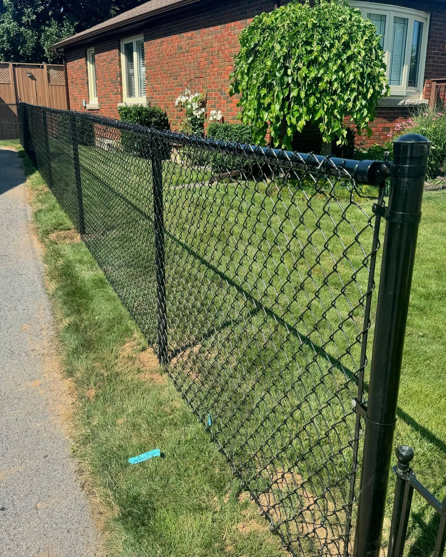 Black metal fence along a green grassy path with trees in the background
