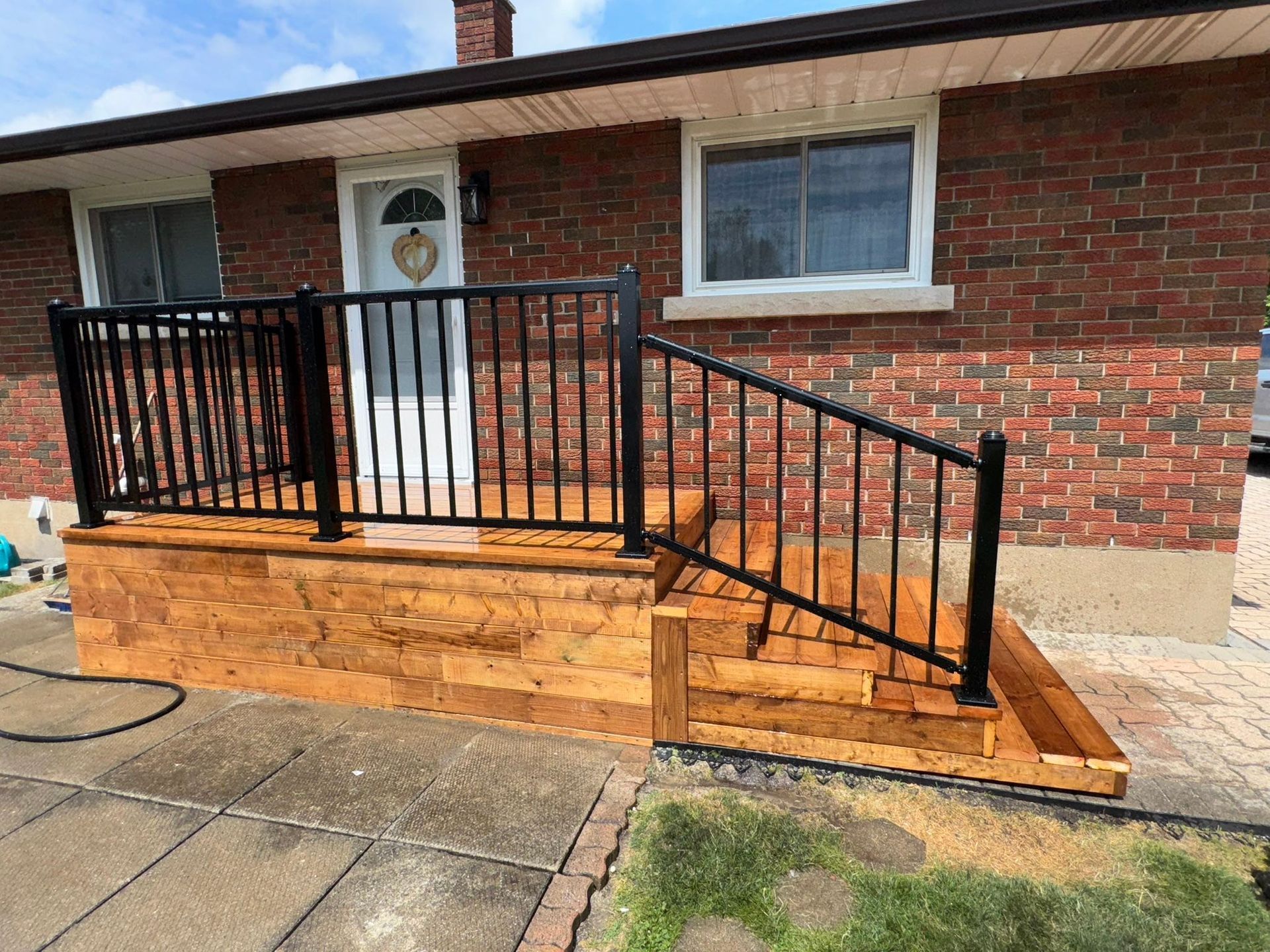 Raised wooden deck with white railing and stairs beside a house, overlooking a green yard