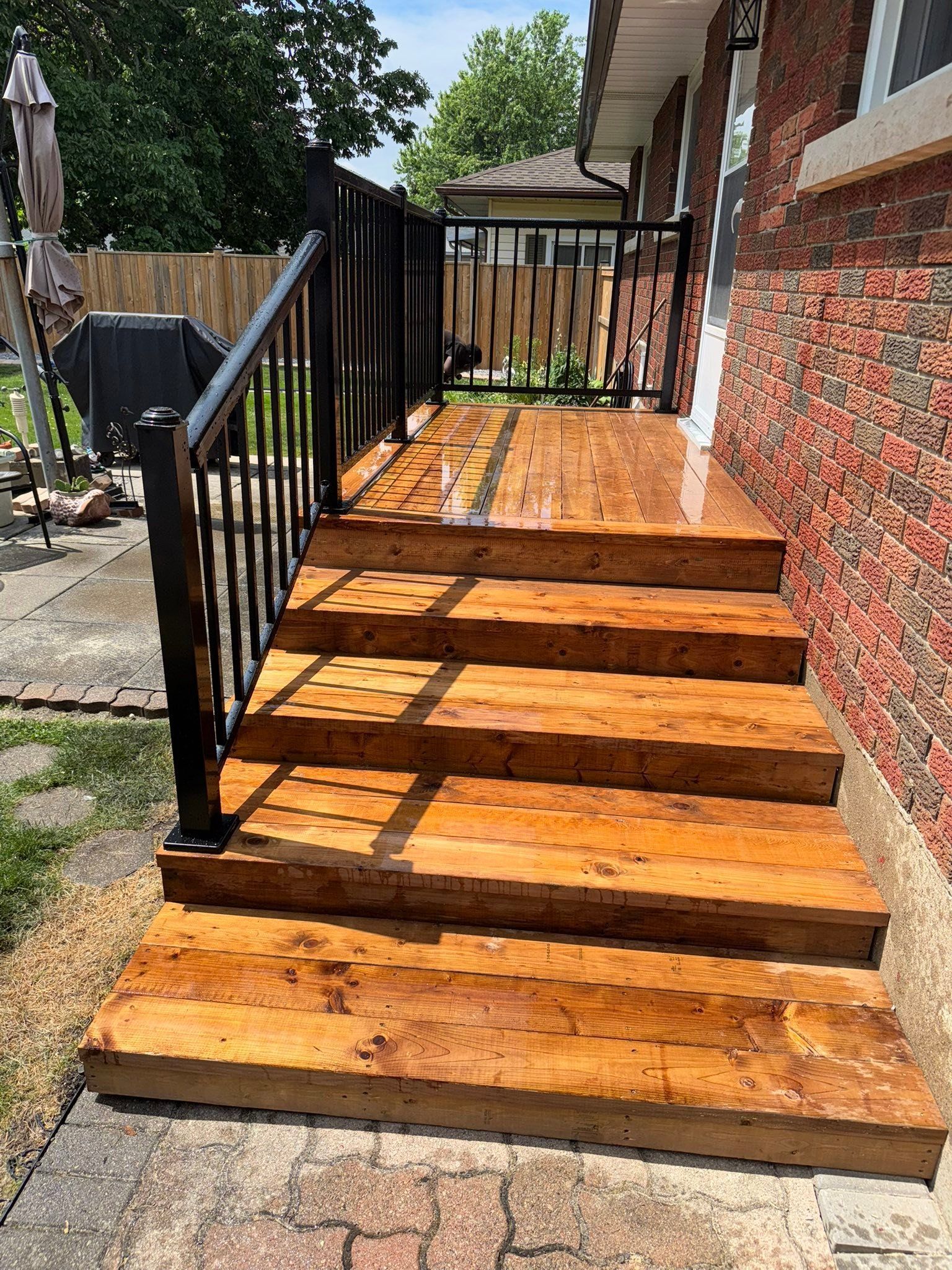 Wooden backyard deck with steps, patio furniture, and an orange umbrella beside a house