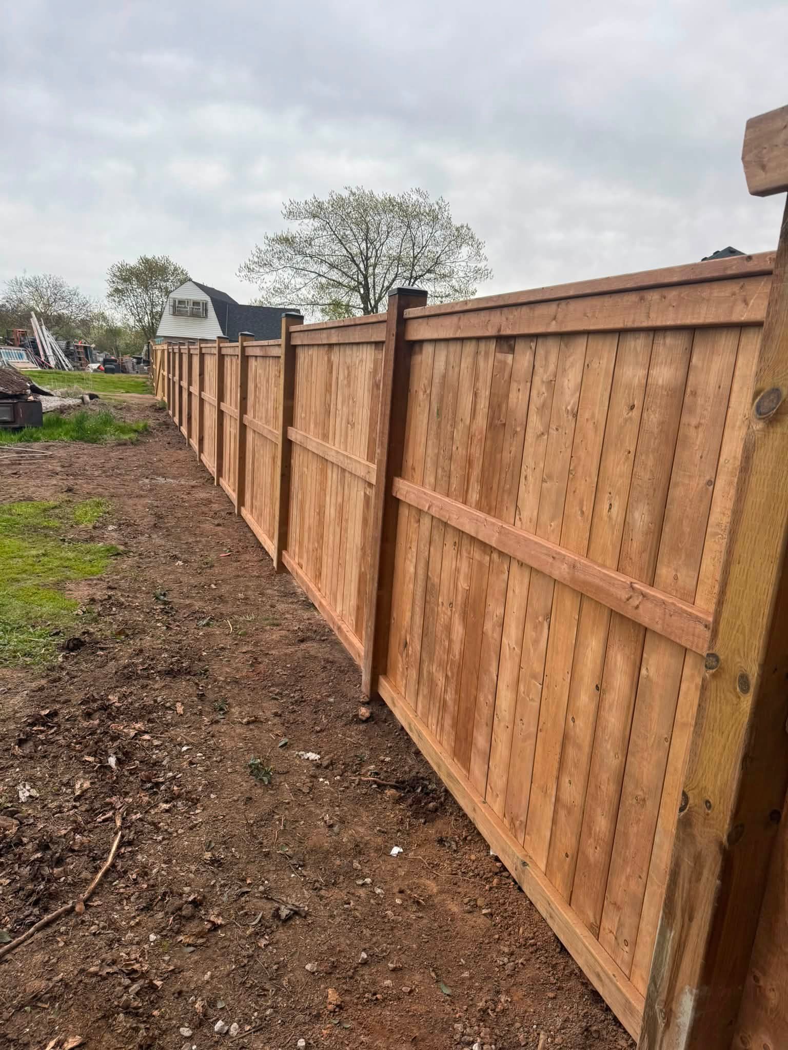 Red wooden fence with lattice top beside a house under a blue sky, bordered by green grass