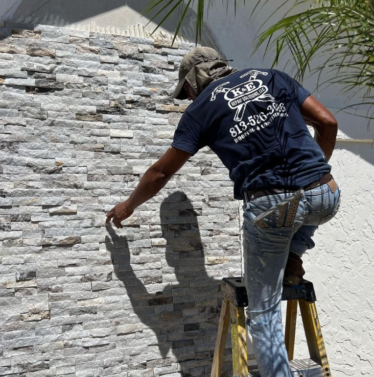 Man on ladder, installing stone veneer on a wall outdoors.