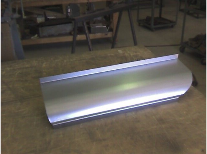 Sheet metal panel on a workbench, silver with a curved edge and folded sides.