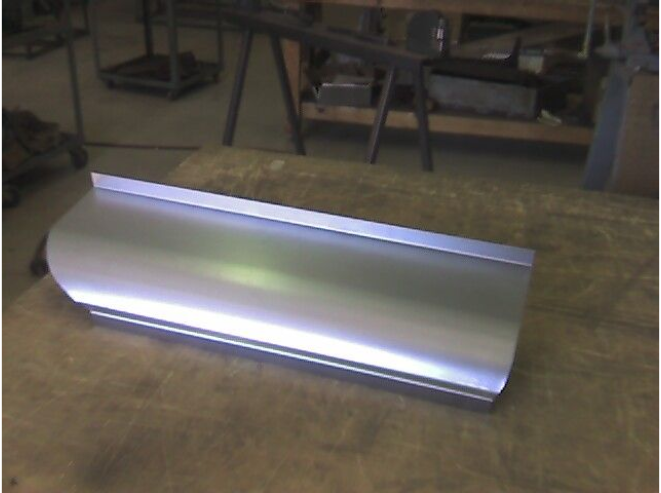 Silver metal automotive body panel on a wooden work surface.