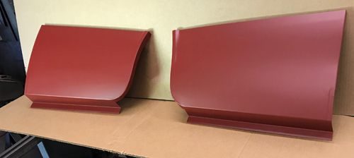 Two red metal car body panels, positioned side by side, on a cardboard surface.