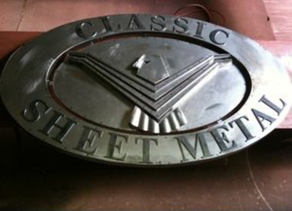 Classic Sheet Metal sign on a brick wall, features silver oval frame with blue lettering and a stylized blue