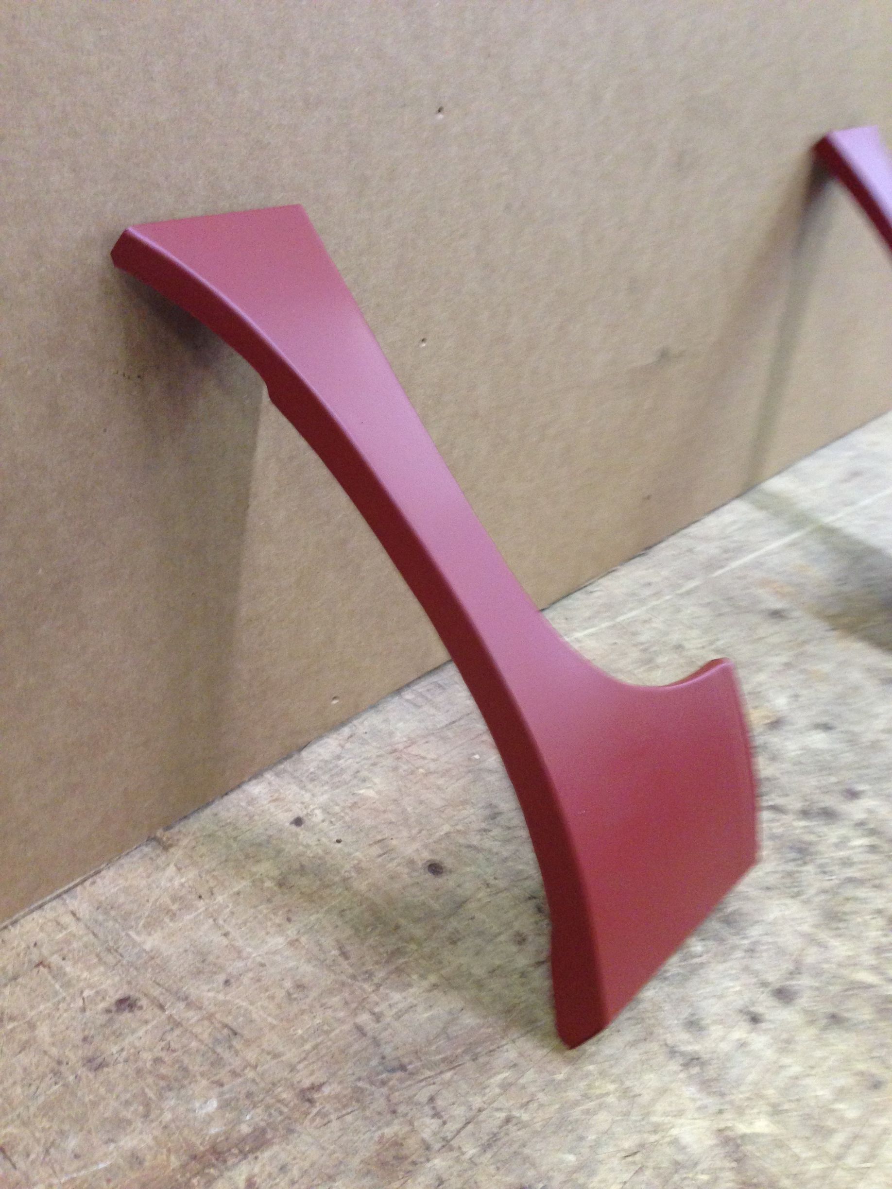 Red curved car interior trim piece leaning against cardboard.