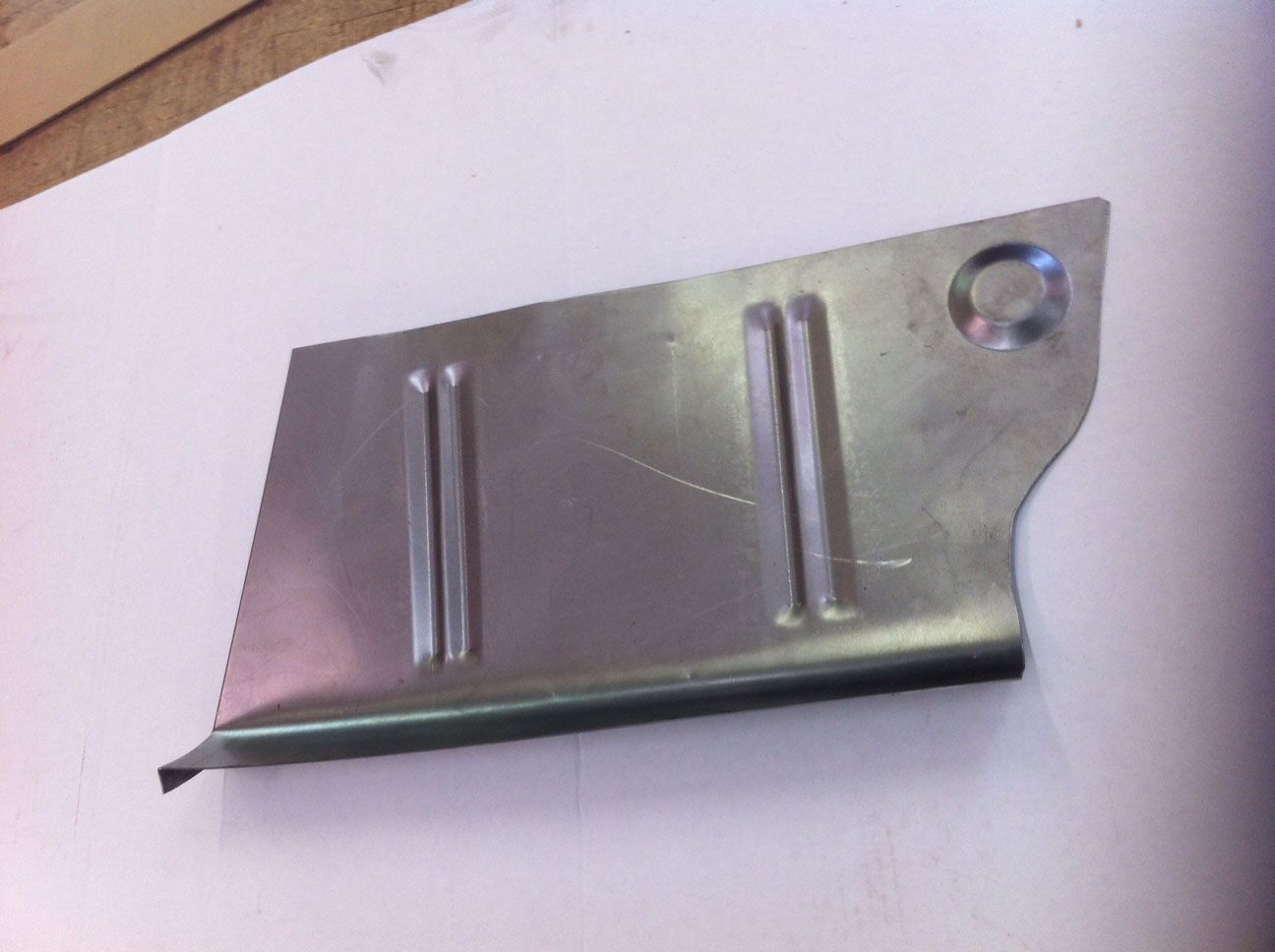 Metal car floor panel with two raised ribs and a circular indent.
