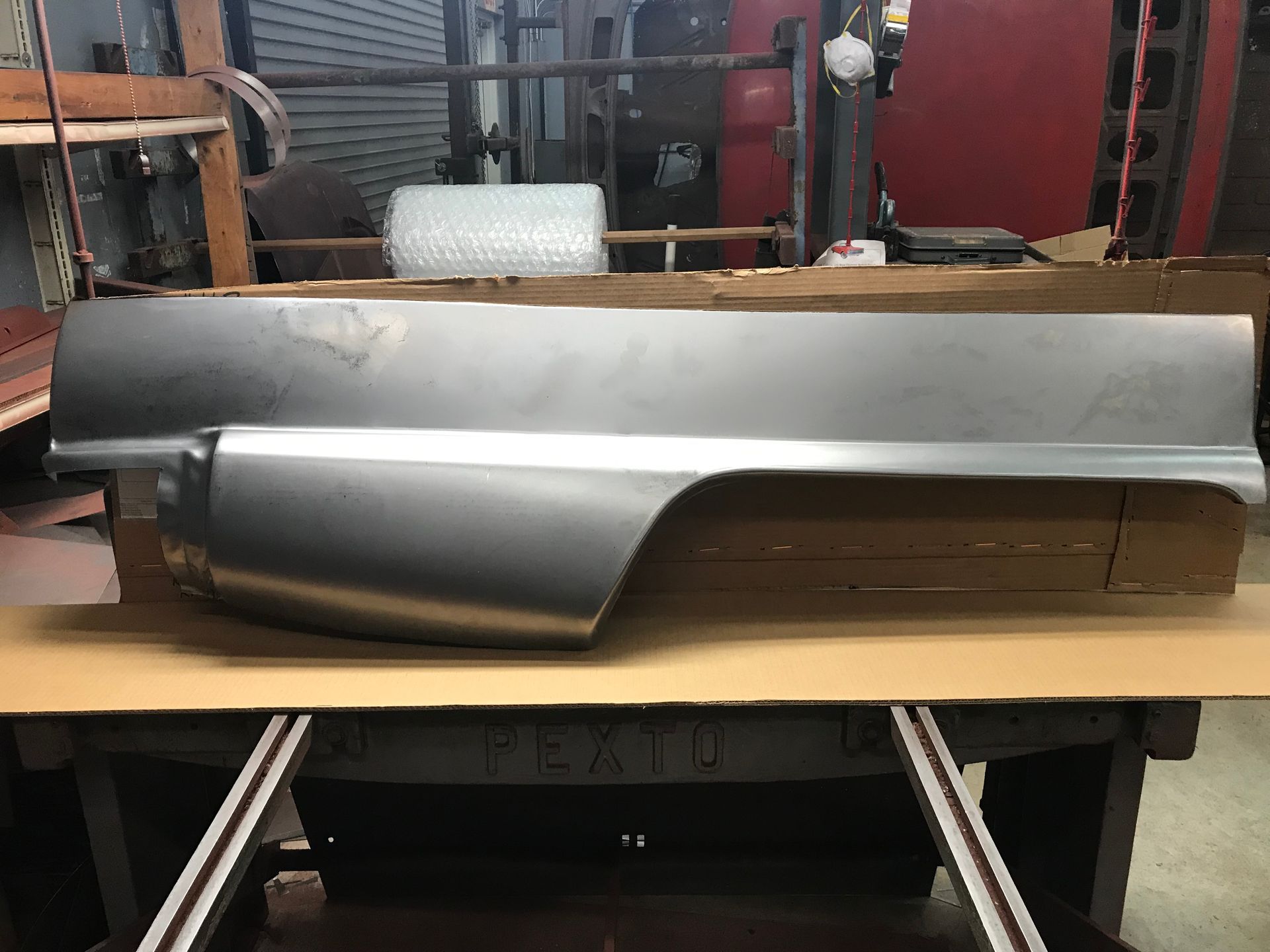 Metal car quarter panel on a work table in a shop.