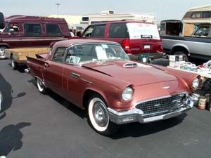 A classic copper-colored Ford Thunderbird with white-walled tires parked at an outdoor car show.