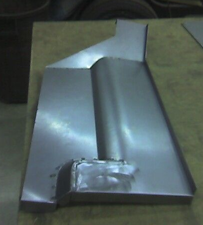 Metal car part, likely a floor pan section, on a wooden surface.