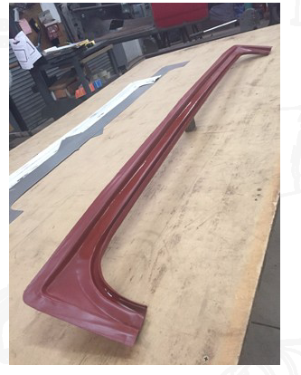 Red car body part on a wooden table, in an industrial setting.