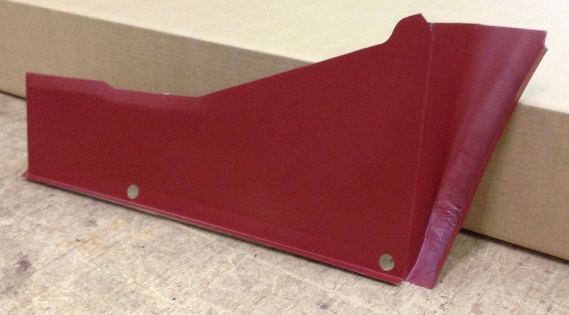 Red car interior panel with two holes, resting on a wooden surface near a cardboard box.