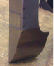 Close-up of a damaged dark brown rectangular structure with a chipped, uneven bottom edge.