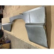 Metal car fender on a wooden surface, showing the curve of a wheel well and a squared-off body panel.