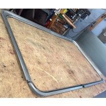 Metal-framed, triangular glass window pane on a wooden surface, ready for installation.