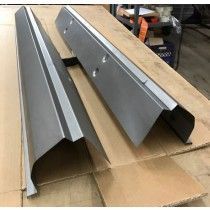 Two metal car rocker panels, gray, resting on cardboard in a workshop.