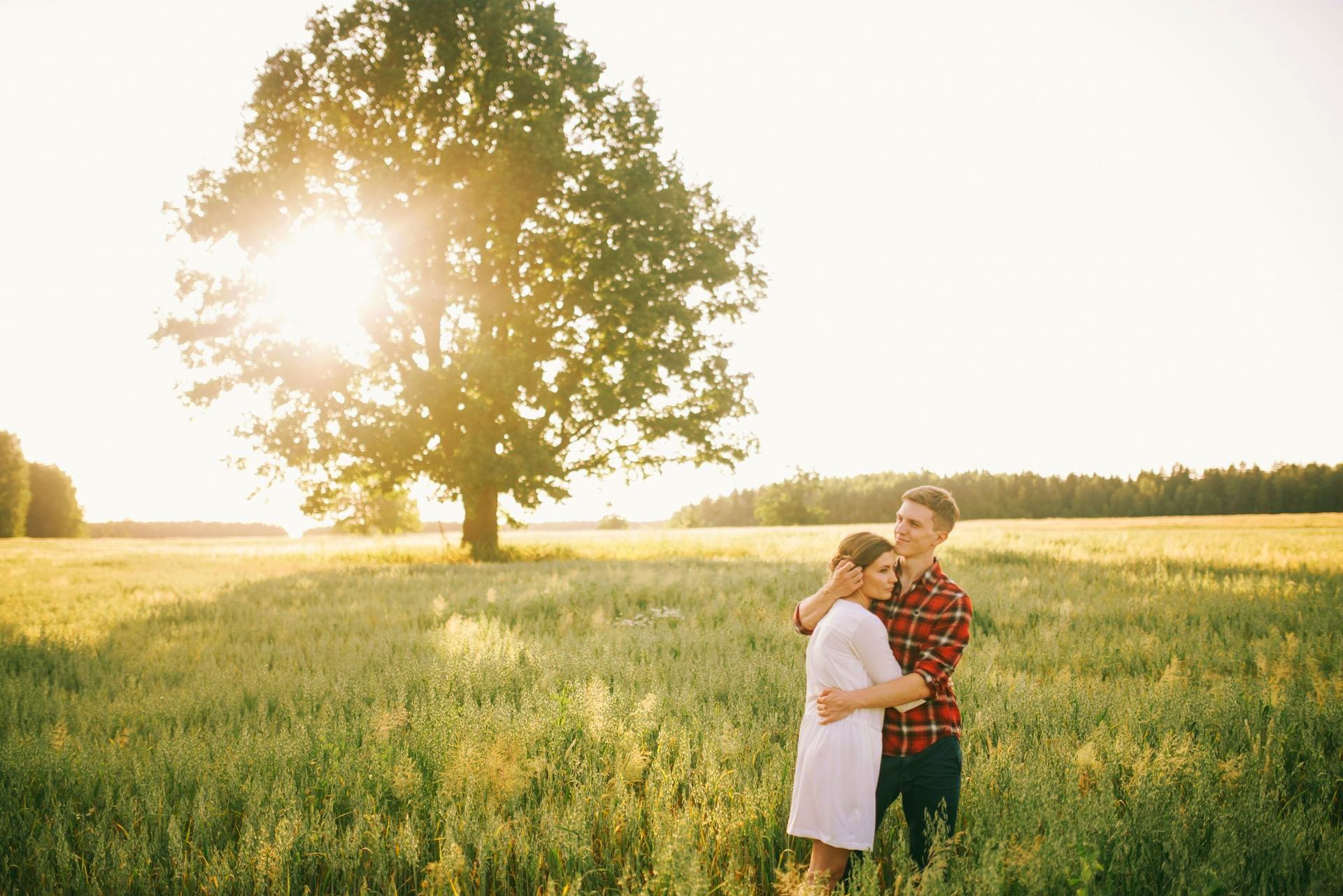 A man and a woman are standing in a field with a tree in the background.