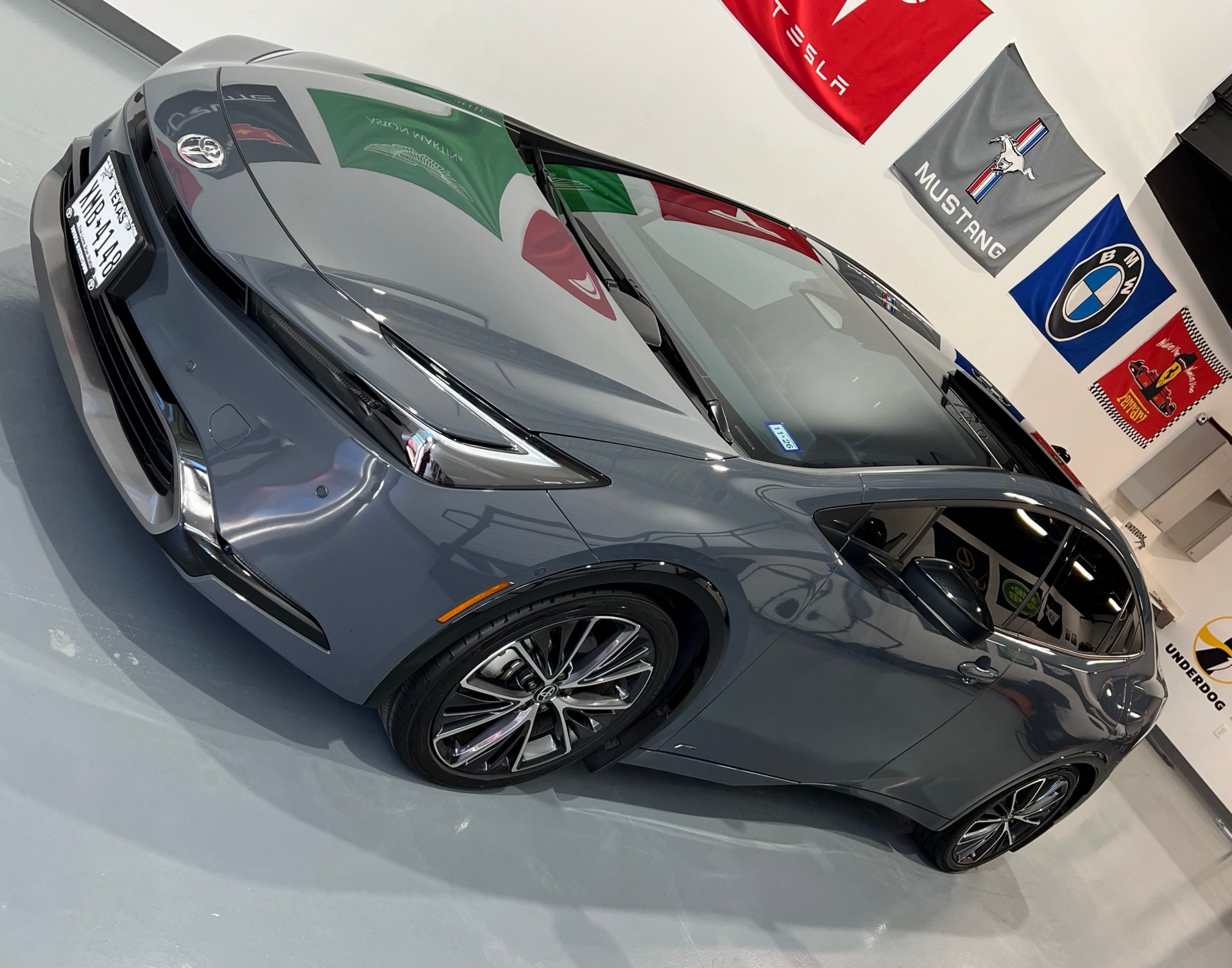 Gray Toyota Prius parked in a garage, with flags of Mexico, Italy, and car brands on the wall.