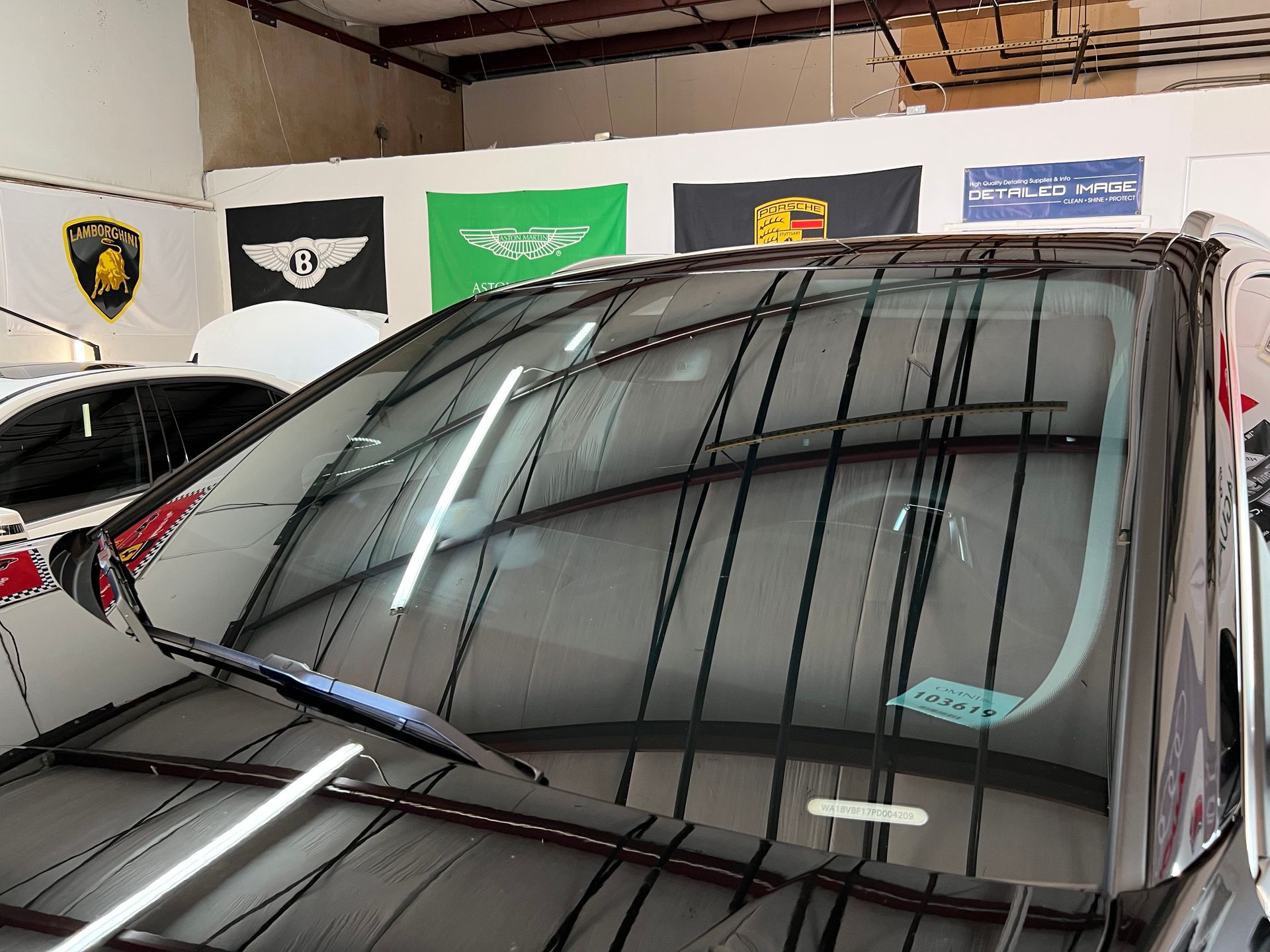 A black car in a garage with windshield wipers up. Flags of different brands are visible in the background.