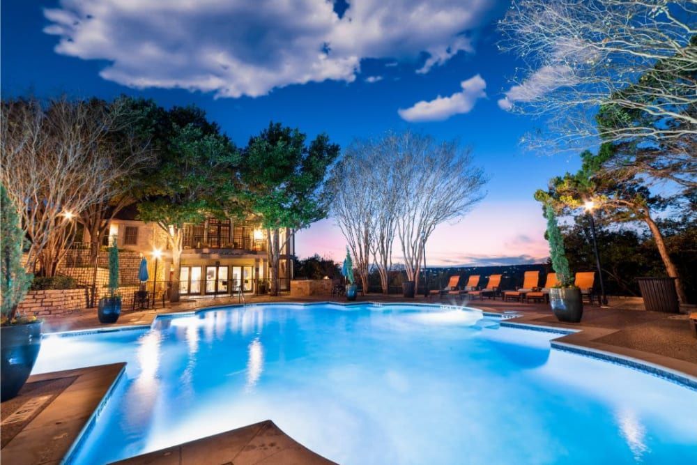 A large swimming pool is lit up at night with the clubhouse building in the background at Marquis at Treetops in Northwest Austin, TX.