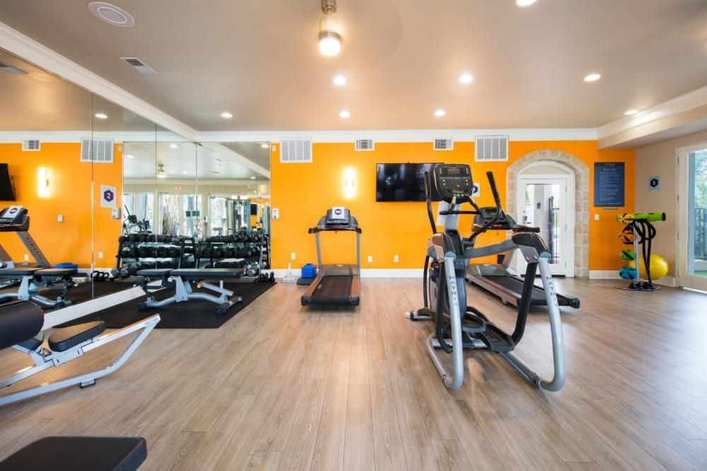 A gym with treadmills, ellipticals, a rowing machine, and a television at Marquis at Treetops in Northwest Austin, TX.