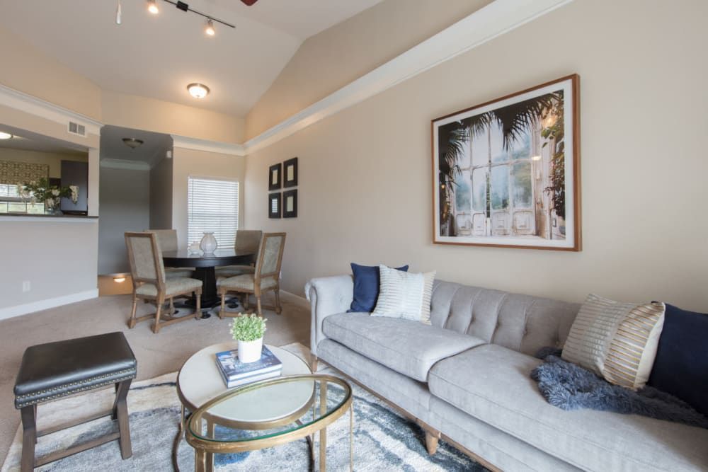 Apartment living room with a couch, table, chairs, and a picture on the wall at Marquis at Treetops in Northwest Austin, TX.