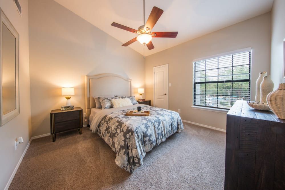 Apartment bedroom with a bed, nightstand, dresser, and ceiling fan at Marquis at Treetops in Northwest Austin, TX.