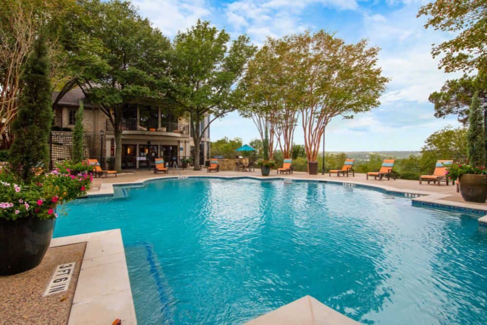 A large swimming pool surrounded by trees and chairs at Marquis at Treetops in Northwest Austin, TX.
