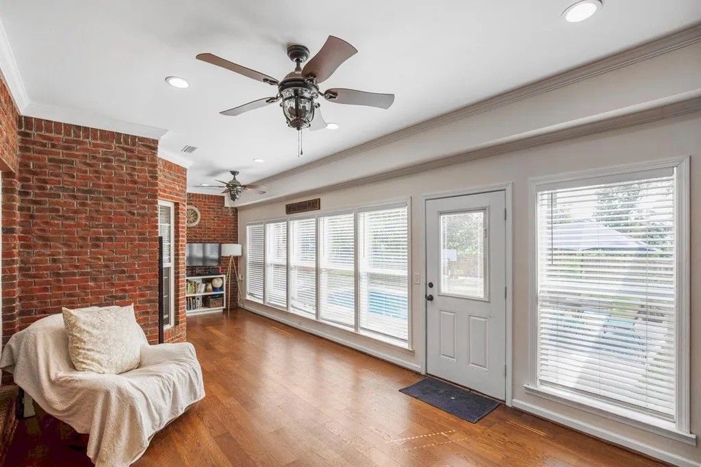 There is a ceiling fan in the living room with a lot of windows.