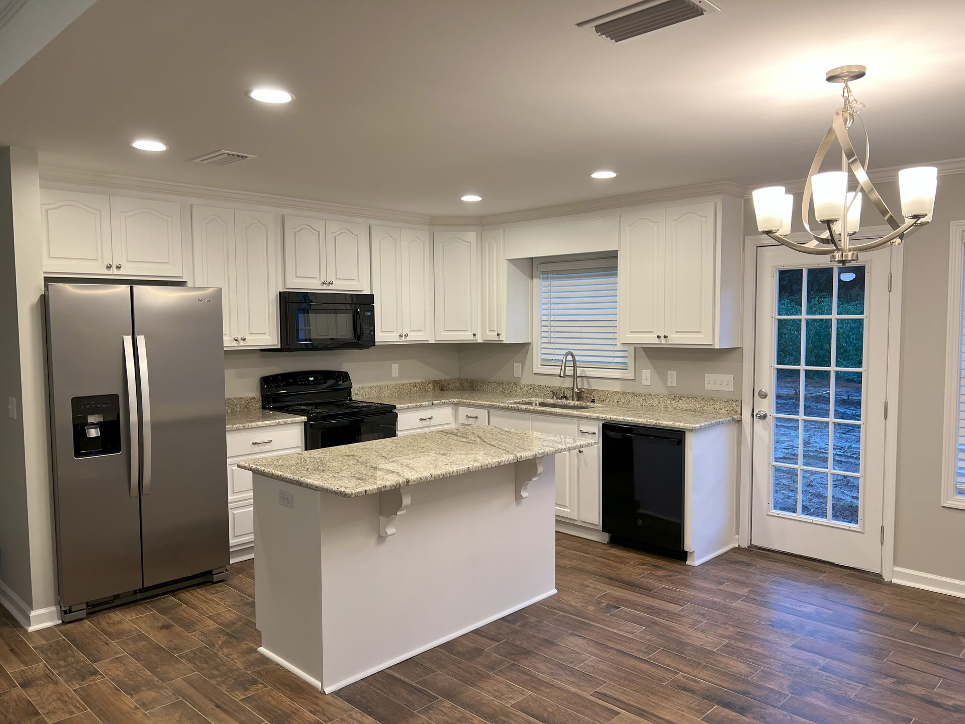 A kitchen with white cabinets , stainless steel appliances , granite counter tops and a large island.