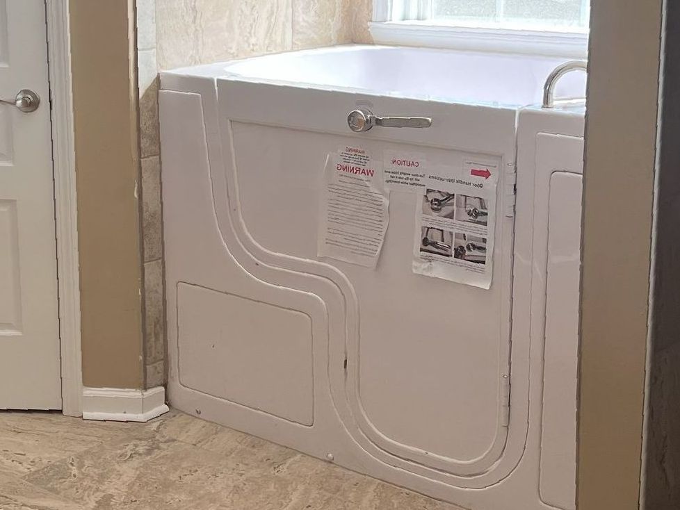 A walk in tub with a door in a bathroom next to a window.