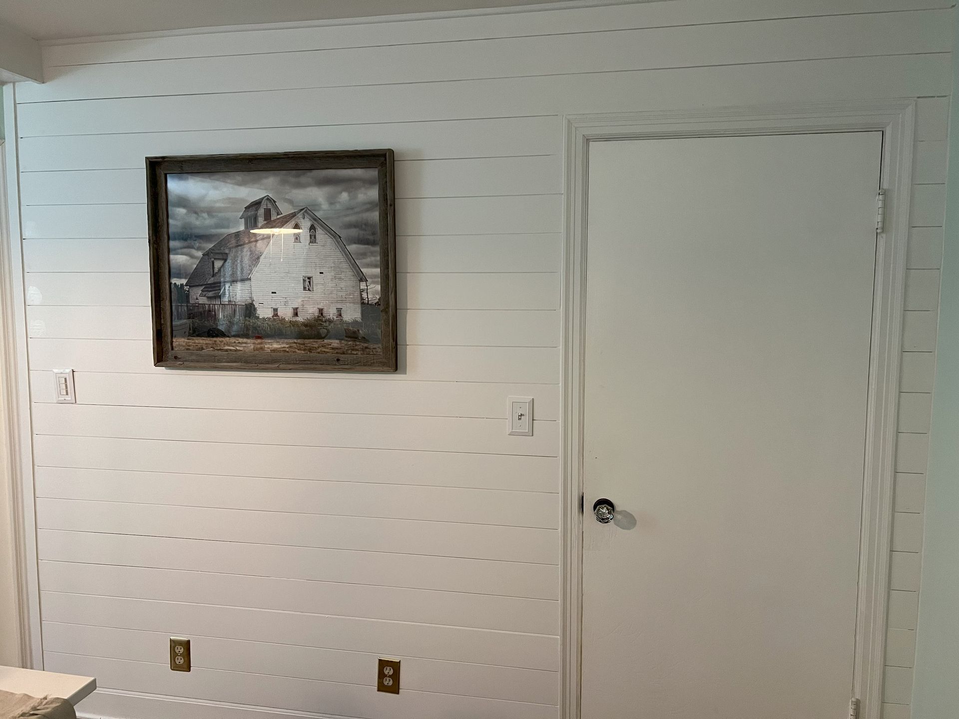 A picture of a barn is hanging on a white wall next to a door.