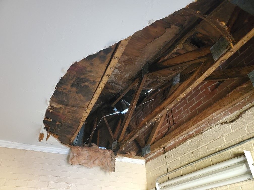 A ceiling with a hole in it and a brick wall behind it.