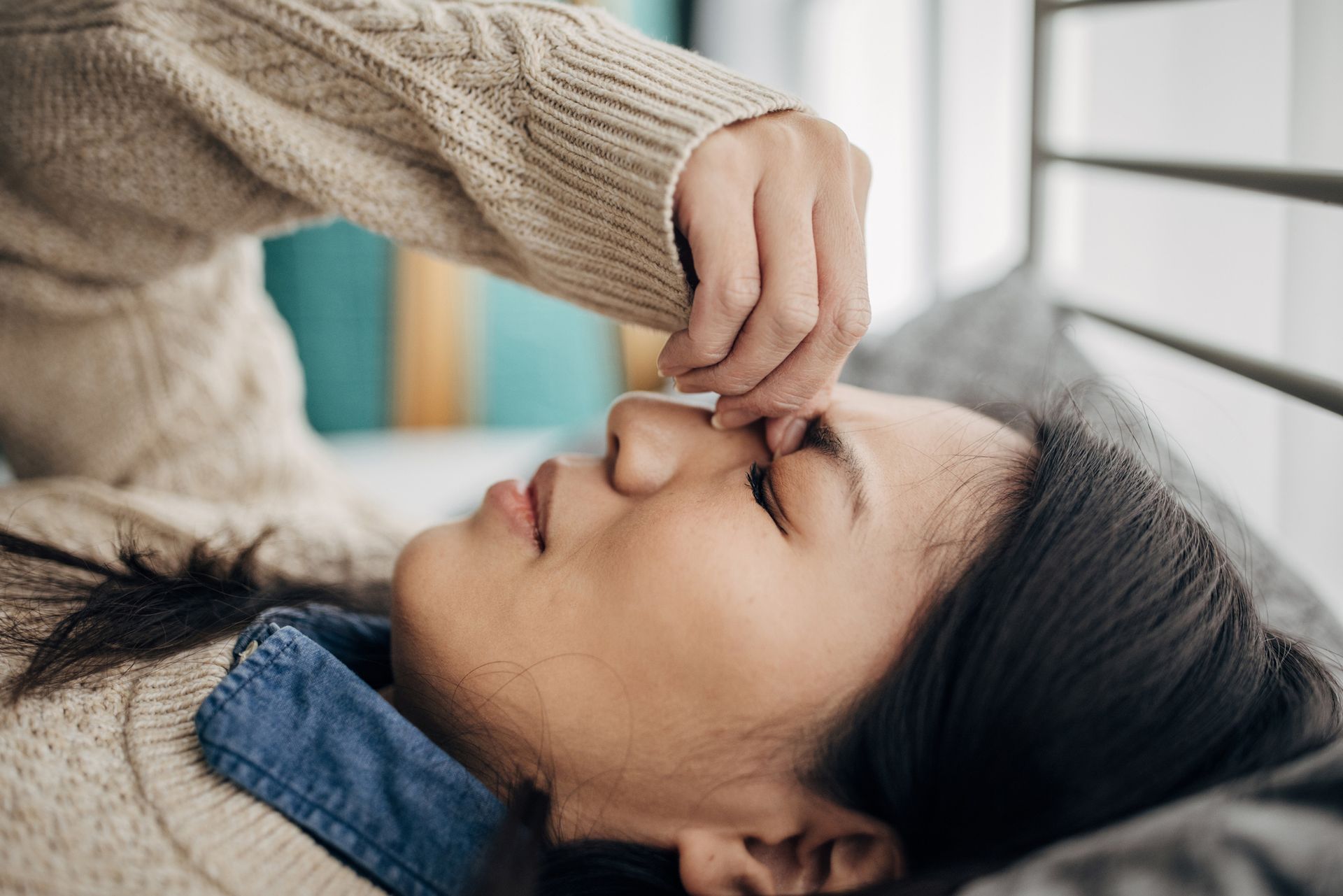 Person lying down with someone touching their forehead. Indoors, neutral colors.