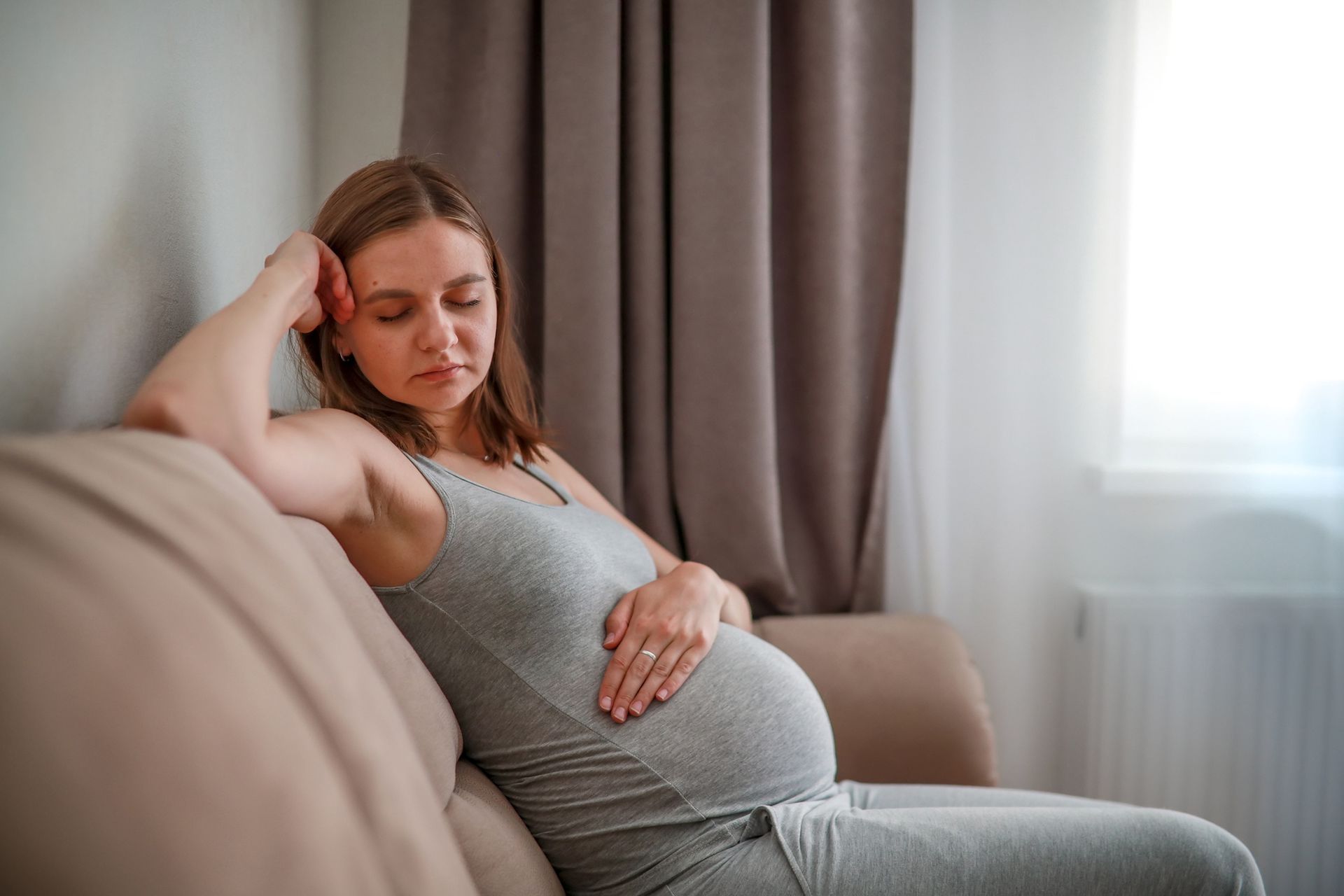 Pregnant person sitting on a couch, resting hand on belly, looking down.
