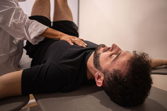 Woman on exercise ball guided by a healthcare provider in a bright living room.