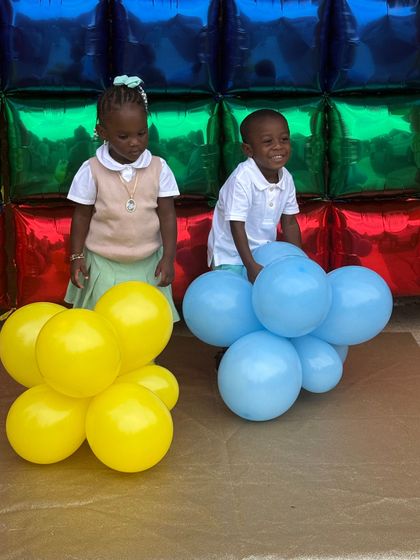 Smiling Black boy at table with colorful blocks; other children and teacher in background.