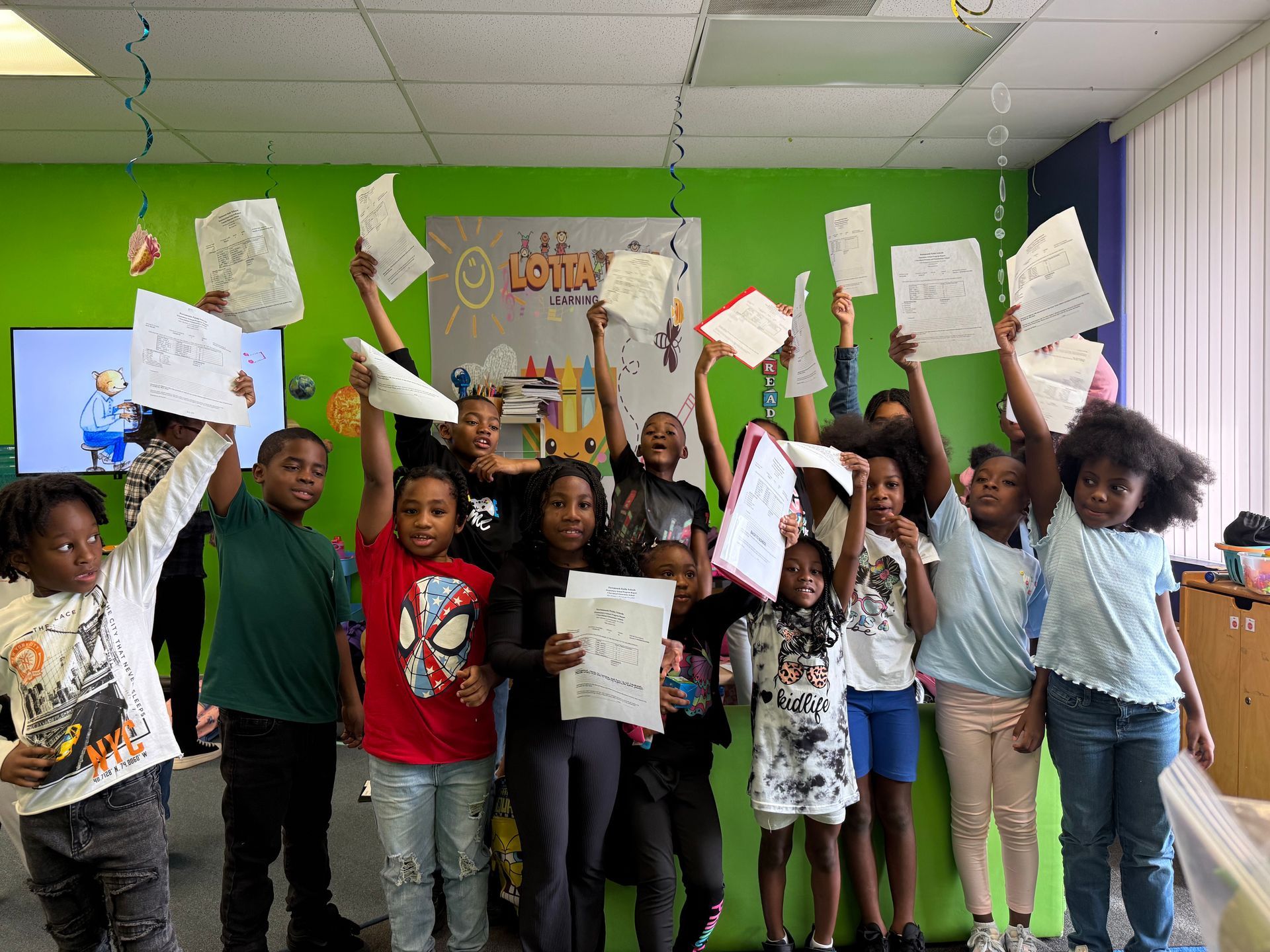 Smiling Black boy at table with colorful blocks; other children and teacher in background.