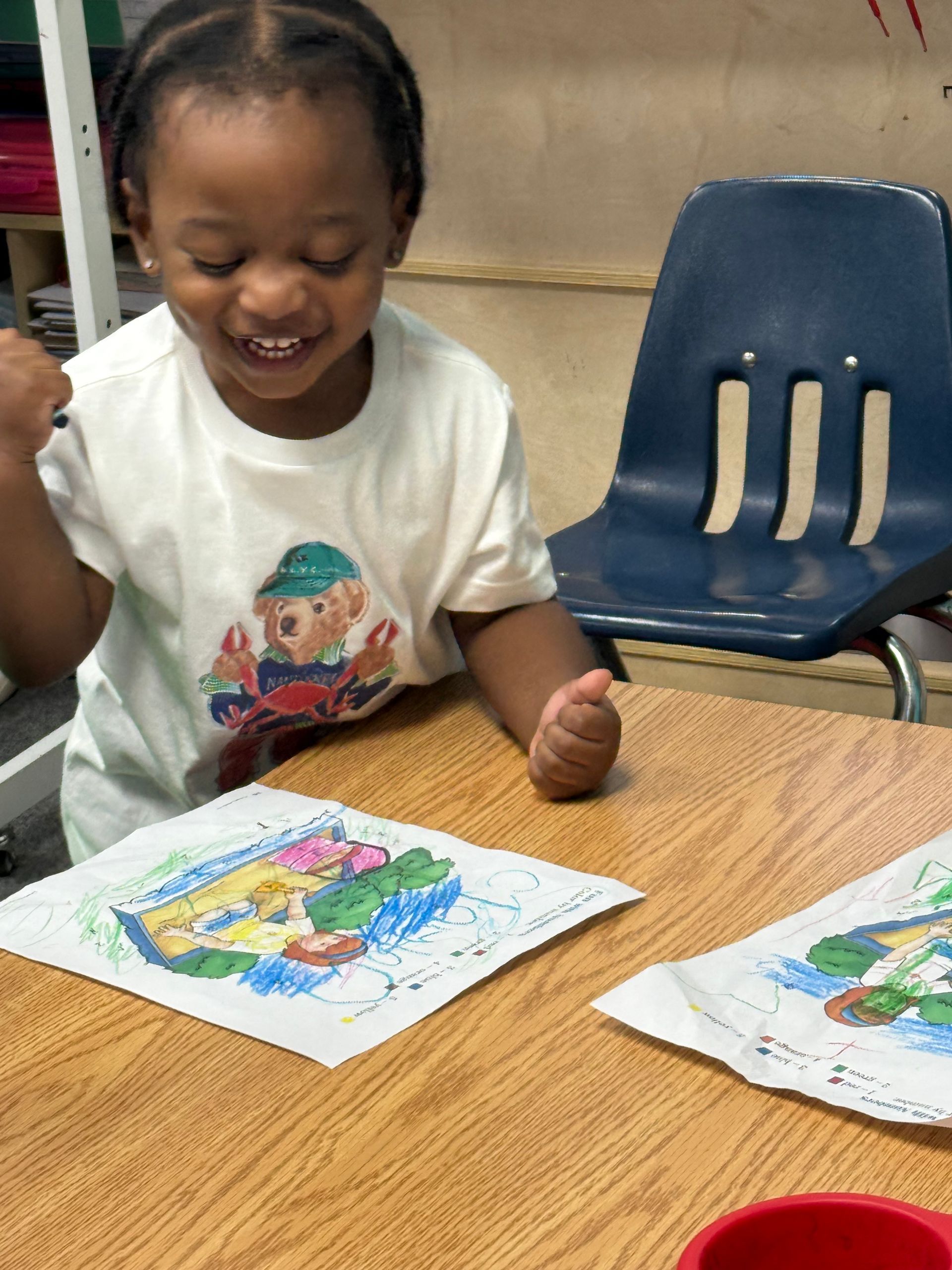 A teacher and six children sit in a circle, arms raised, hands open, in a classroom.