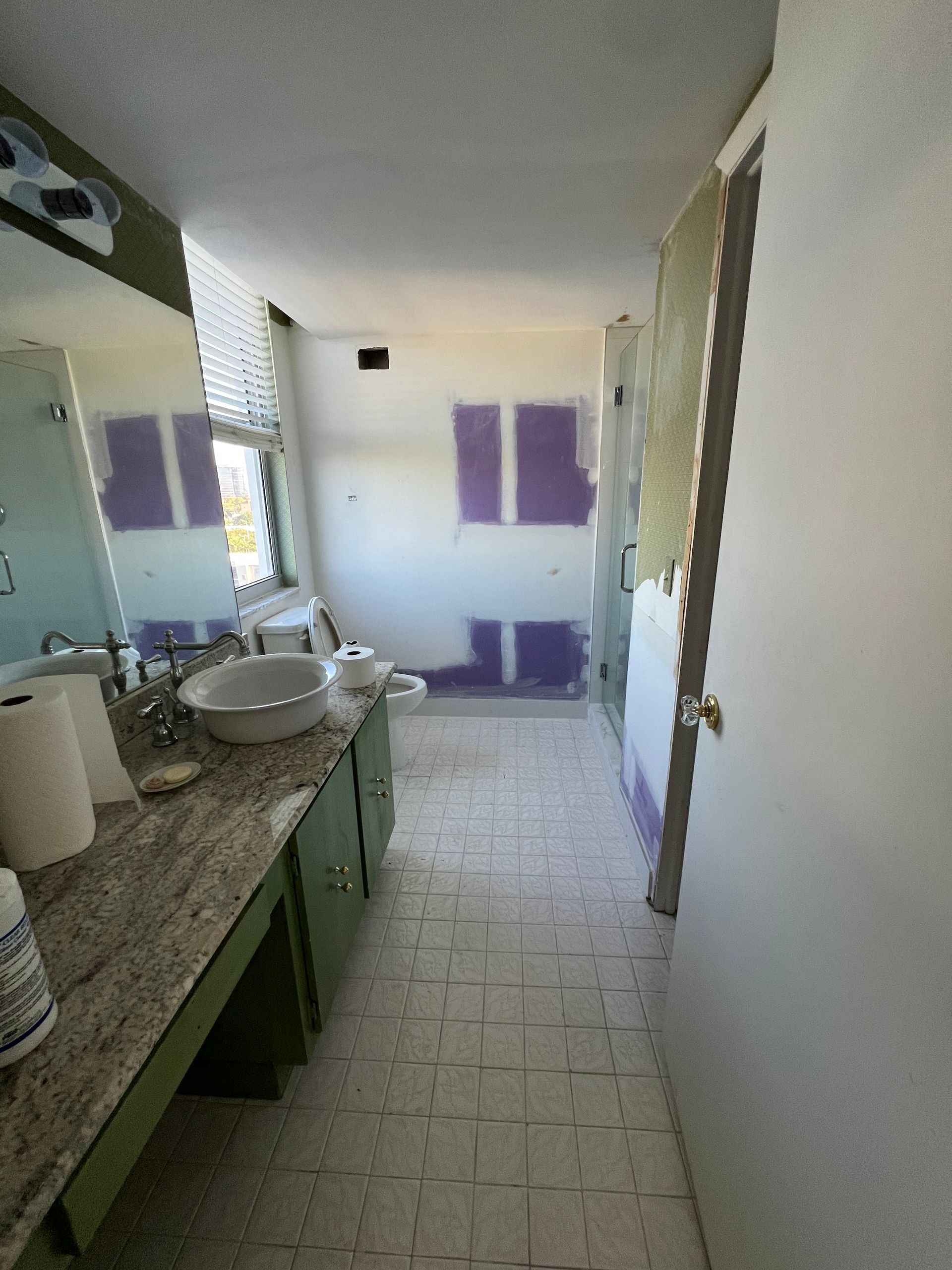 Bathroom under renovation with partially removed wall and green cabinets.