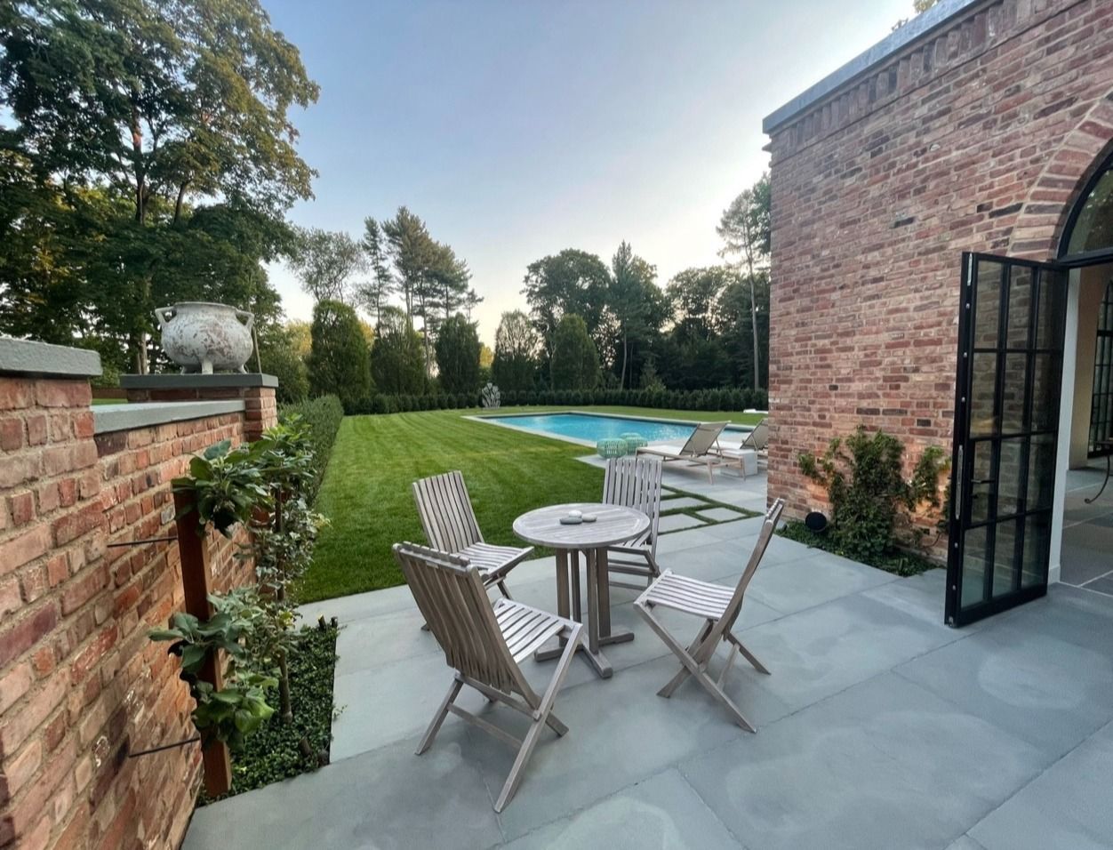 A patio with a table and chairs and a pool in the background