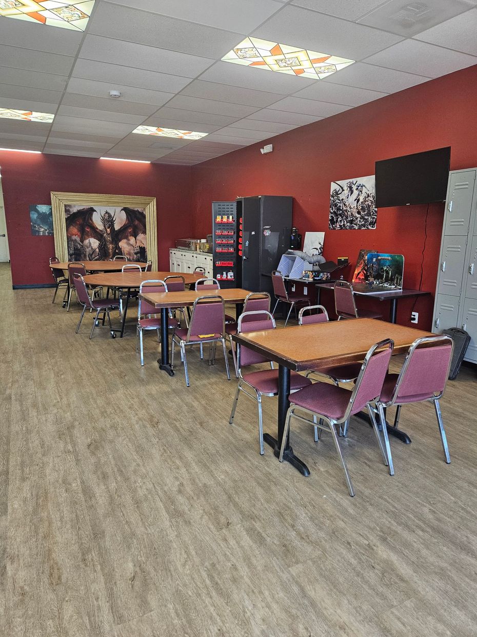 Empty restaurant seating area with red walls, wood floors, and tables and chairs under bright ceiling lights