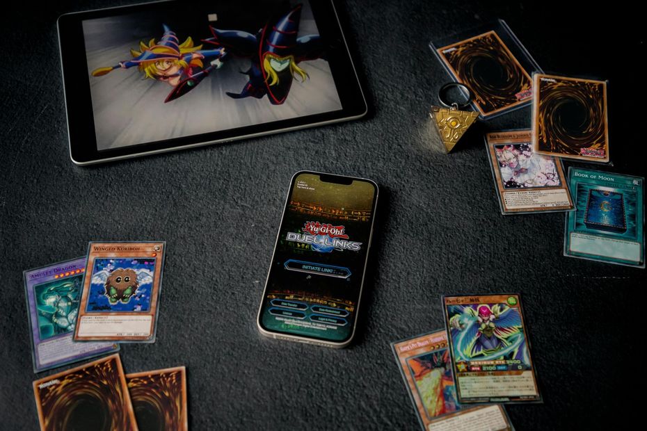 Trading card game setup with cards, a smartphone, and a tablet on a dark tabletop