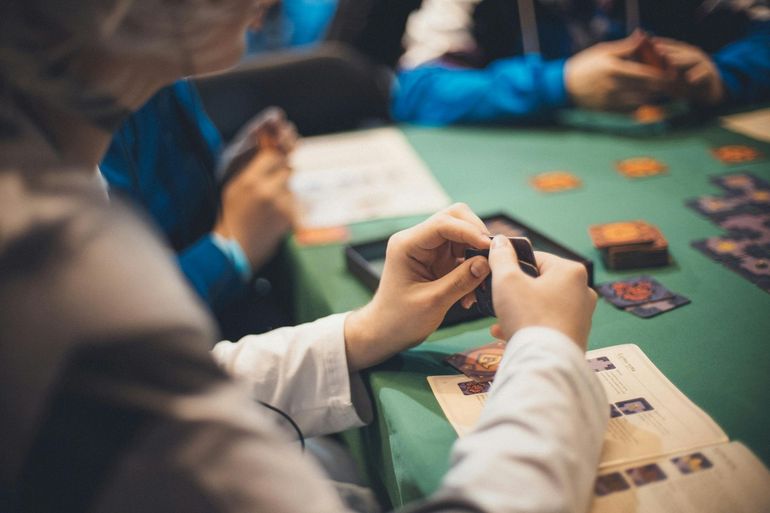 People playing a card game at a green table, with hands holding cards and game pieces in view